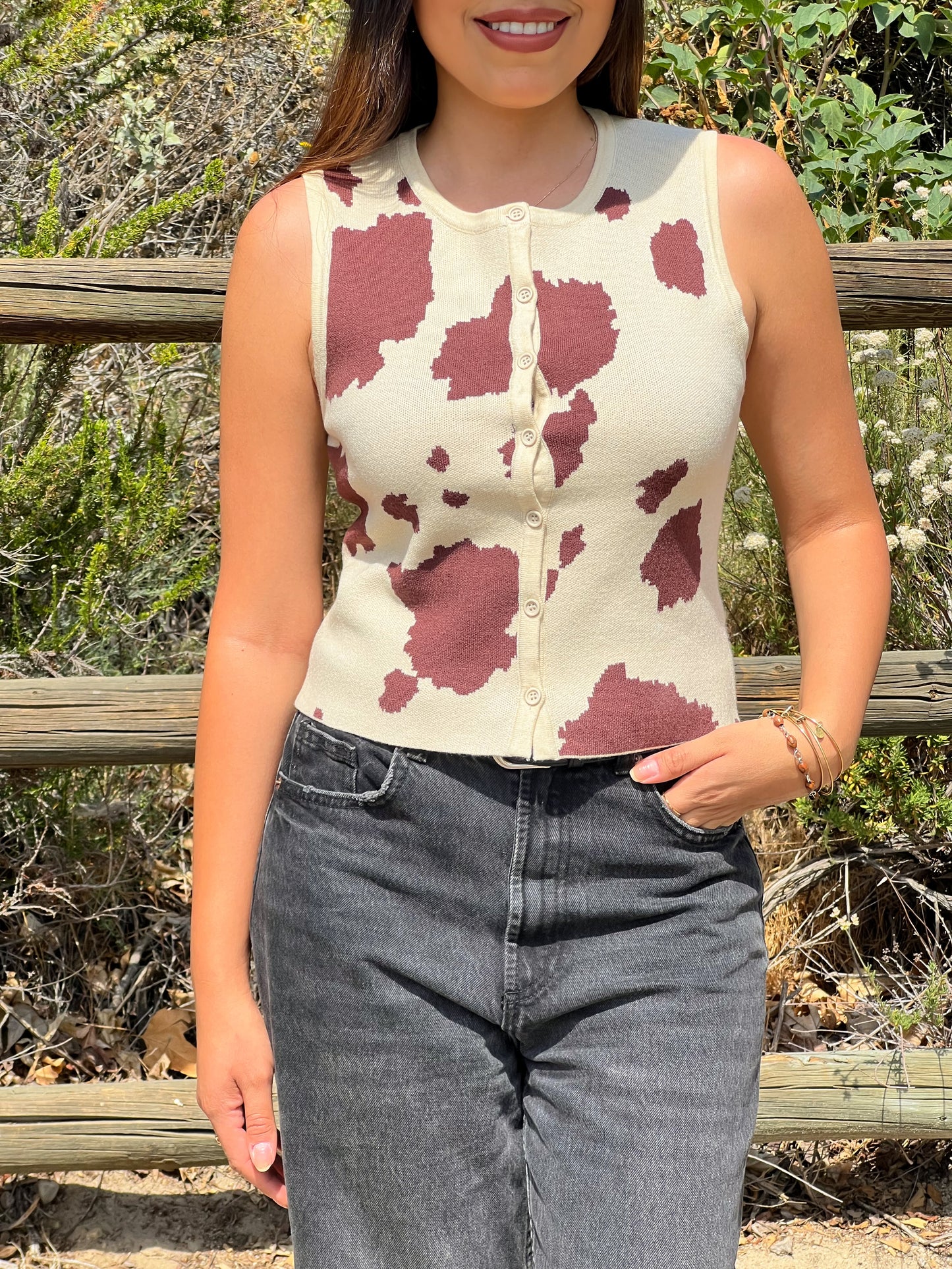 Person wearing a sleeveless top with a cow print design outdoors.