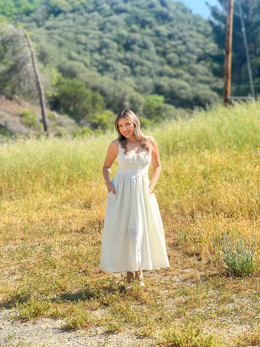 Woman in a white dress standing in a field with trees in the background