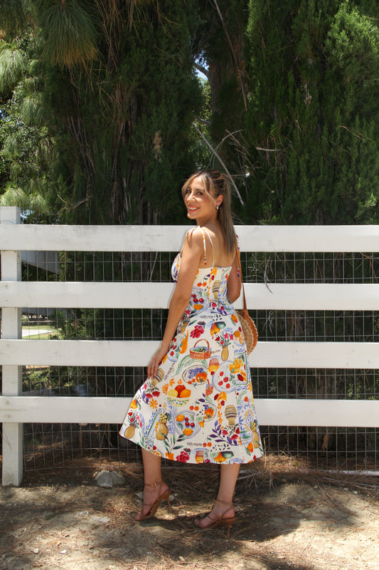 Woman in a floral dress standing in front of a white fence with greenery in the background
