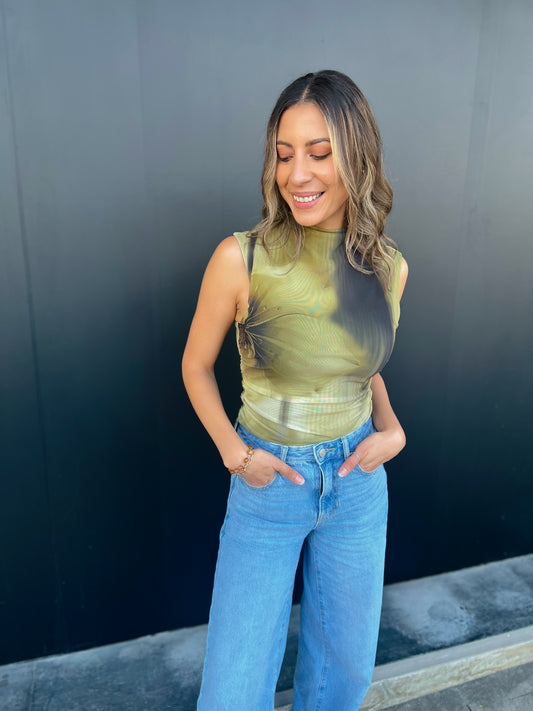 Woman wearing a green sleeveless top and blue jeans against a dark background