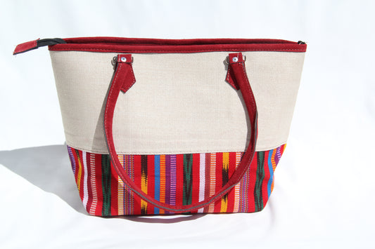 Front view of a handwoven handbag with a bottom panel of intricate Guatemalan fabric with red faux suede shoulder straps and top zipper closure to protect essential items from falling out. the prefect travel, hiking or beach bag unique bag great for your next destination boho bag and hippie style bag a great standout accessories made in Guatemala