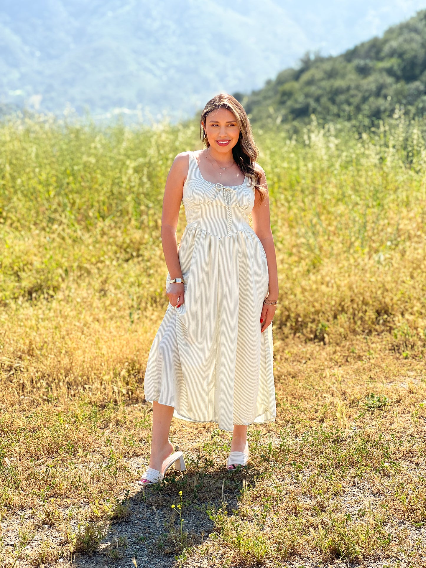 Woman in a white dress standing in a field with mountains in the background