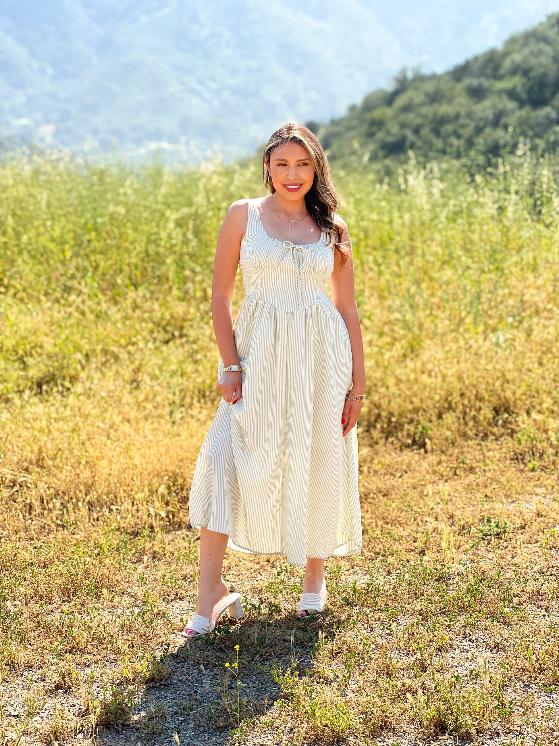 Woman in a white dress standing in a field with mountains in the background