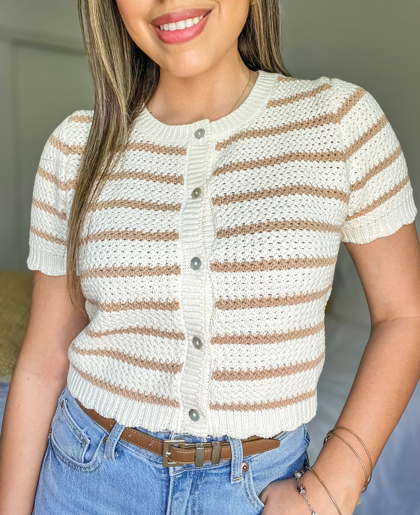 Woman wearing a white and brown striped short-sleeve cardigan with blue jeans.