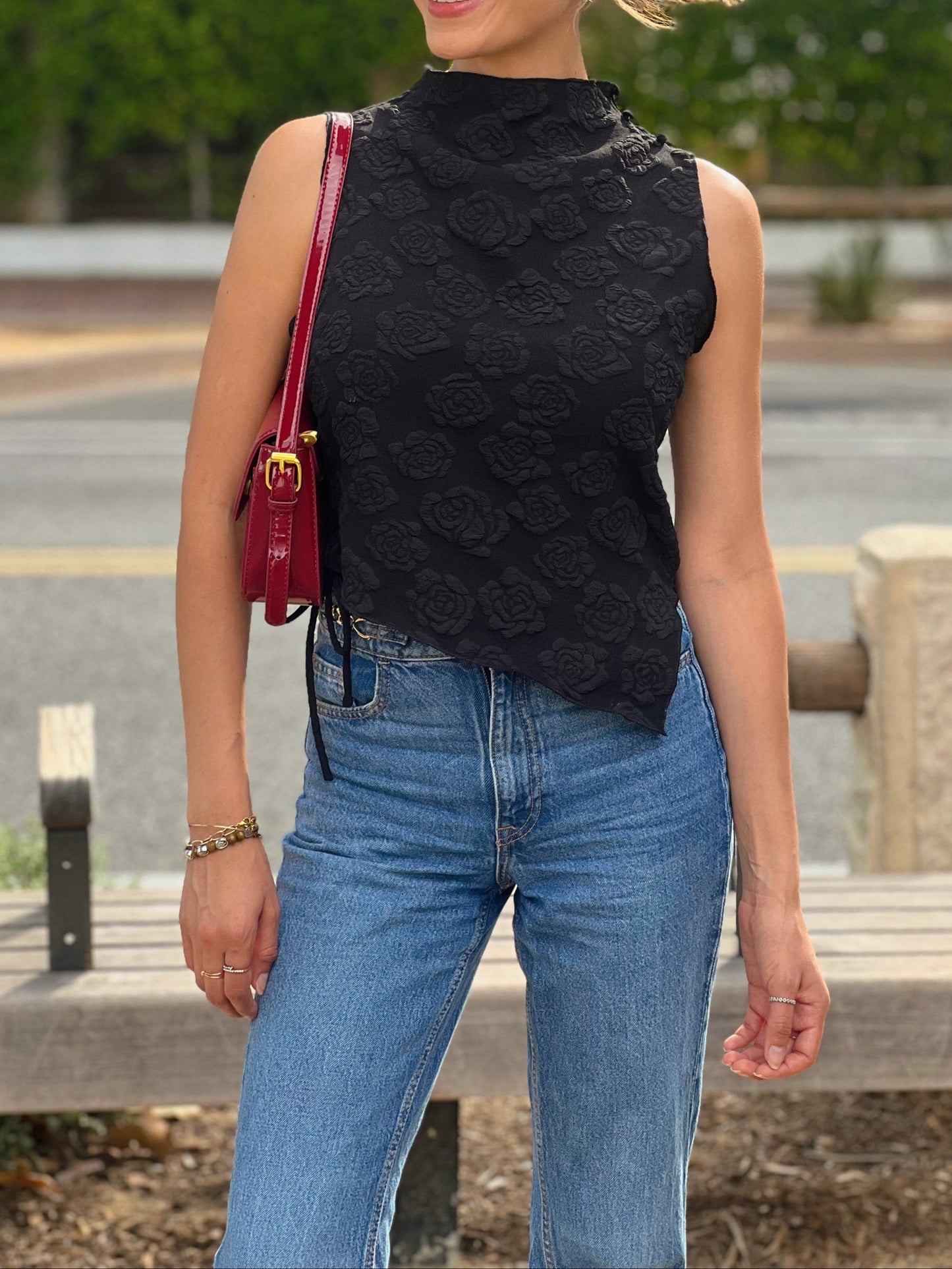 Woman wearing a black sleeveless top and blue jeans, standing outdoors.