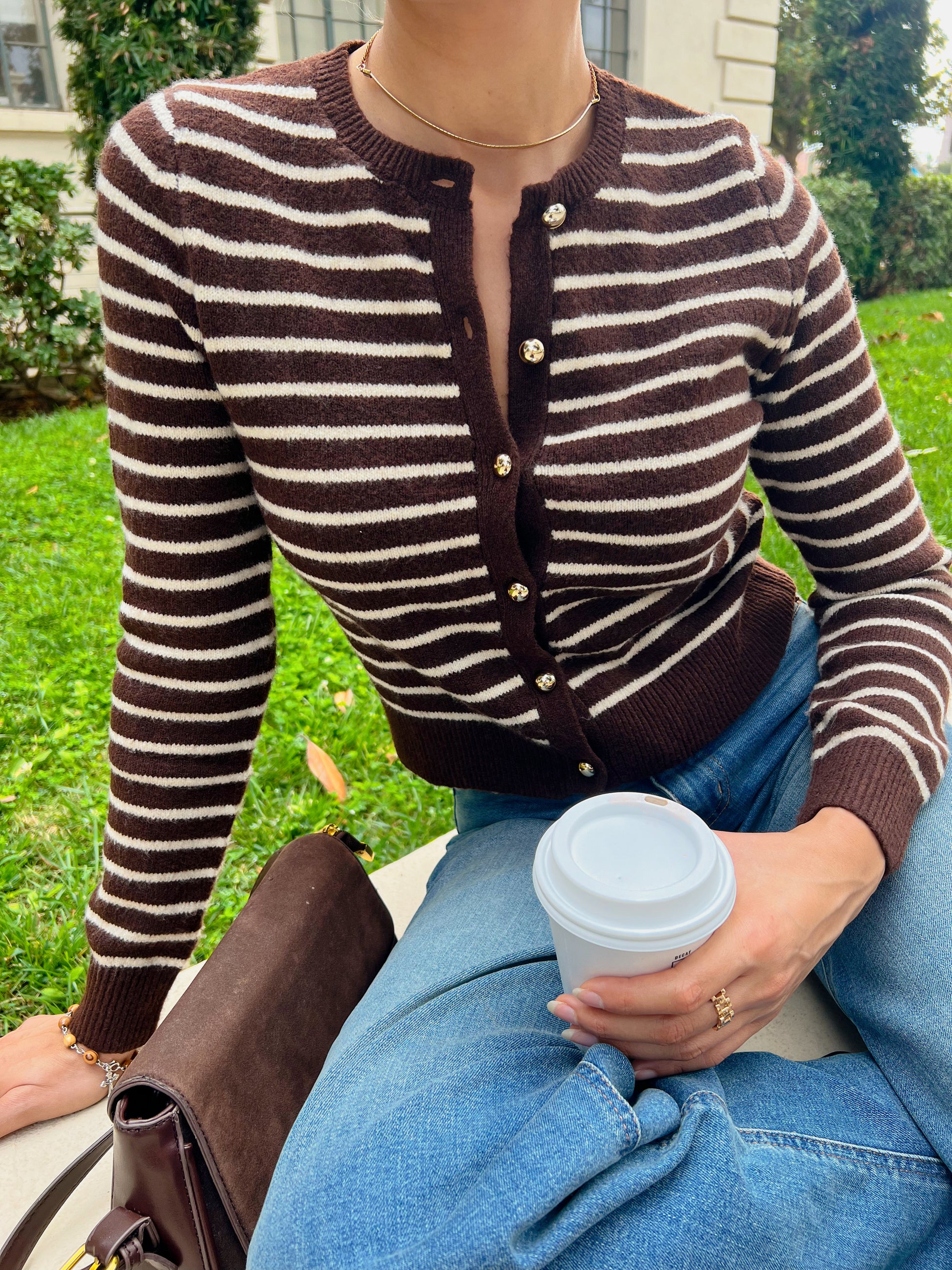 Person wearing a brown and white striped cardigan holding a coffee cup outdoors.