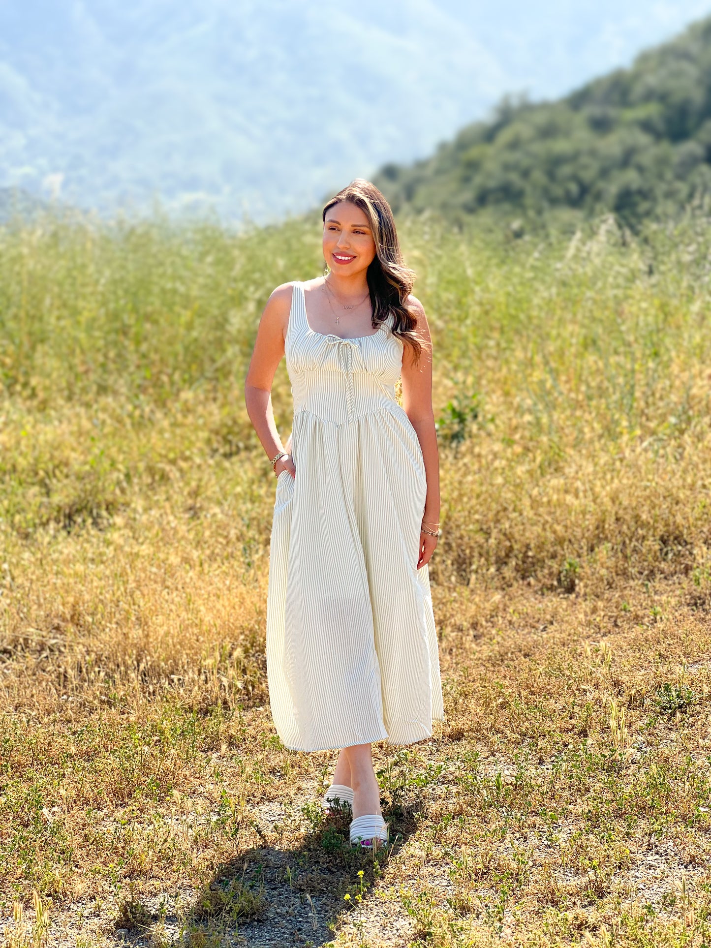 Woman in a white dress standing in a field with mountains in the background