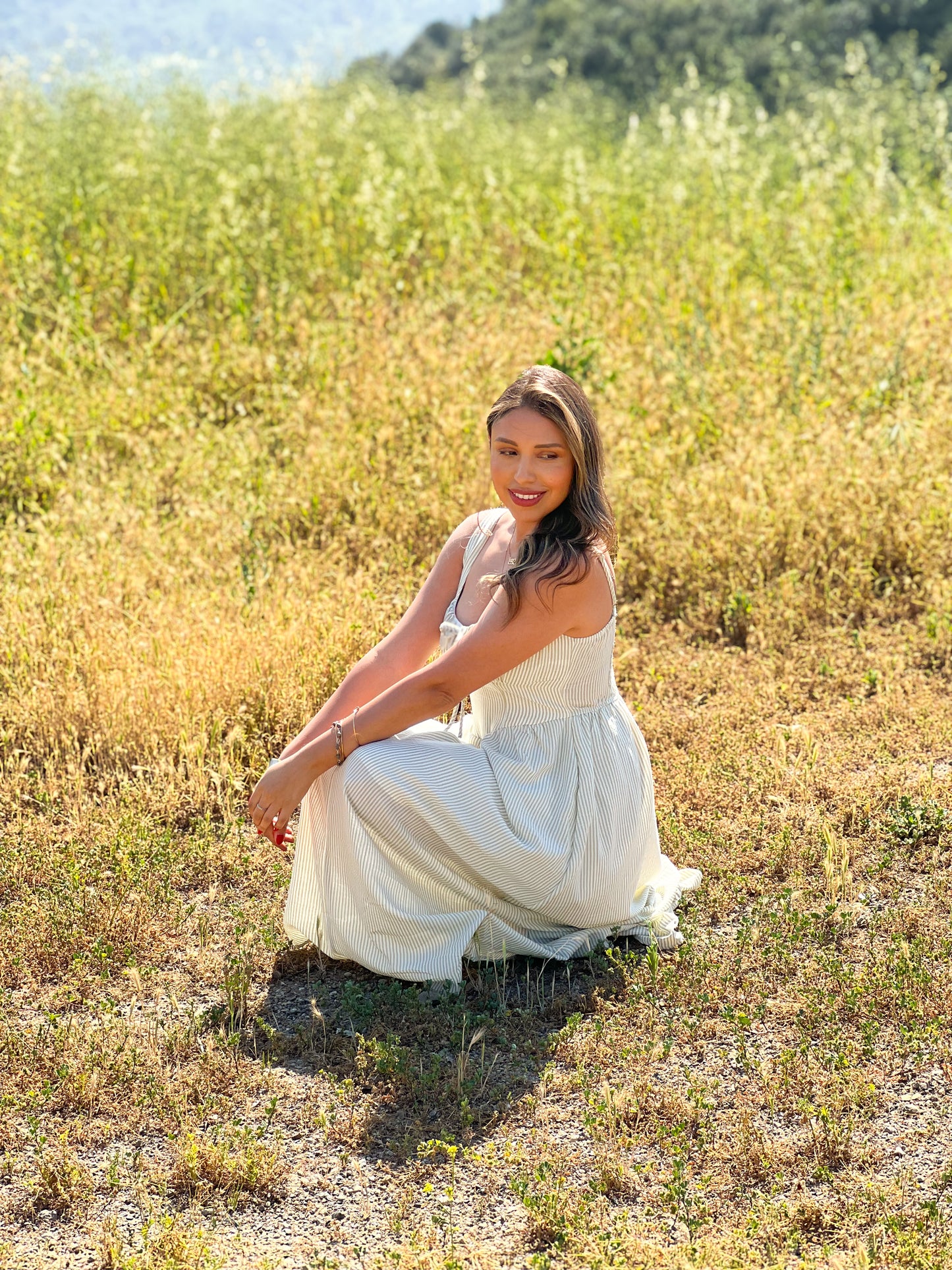 Woman in a white dress sitting in a field of tall grass with mountains in the background