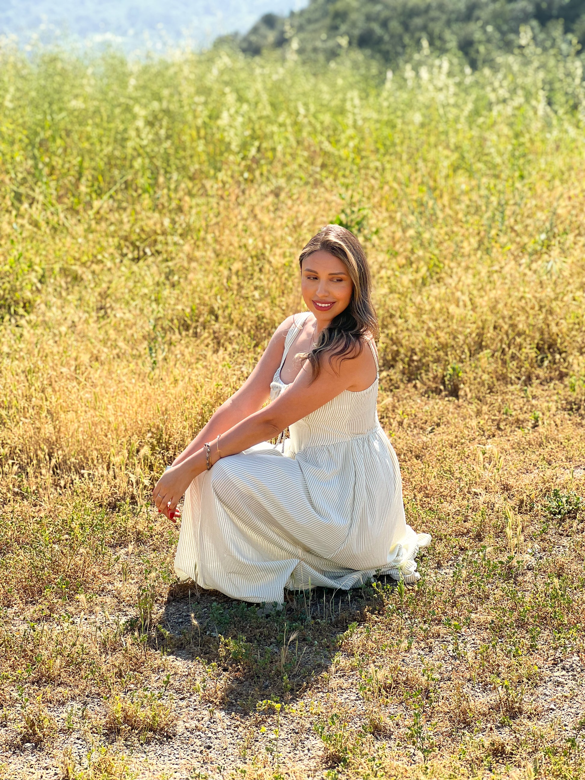 Woman in a white dress sitting in a field of tall grass with mountains in the background