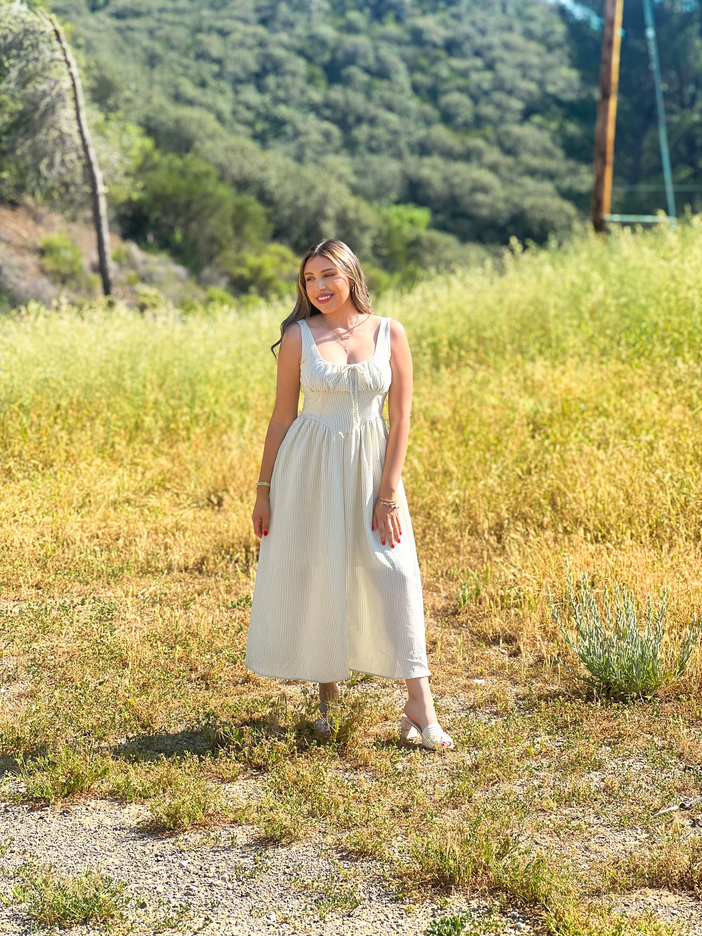 Woman in a white dress standing in a field with mountains in the background