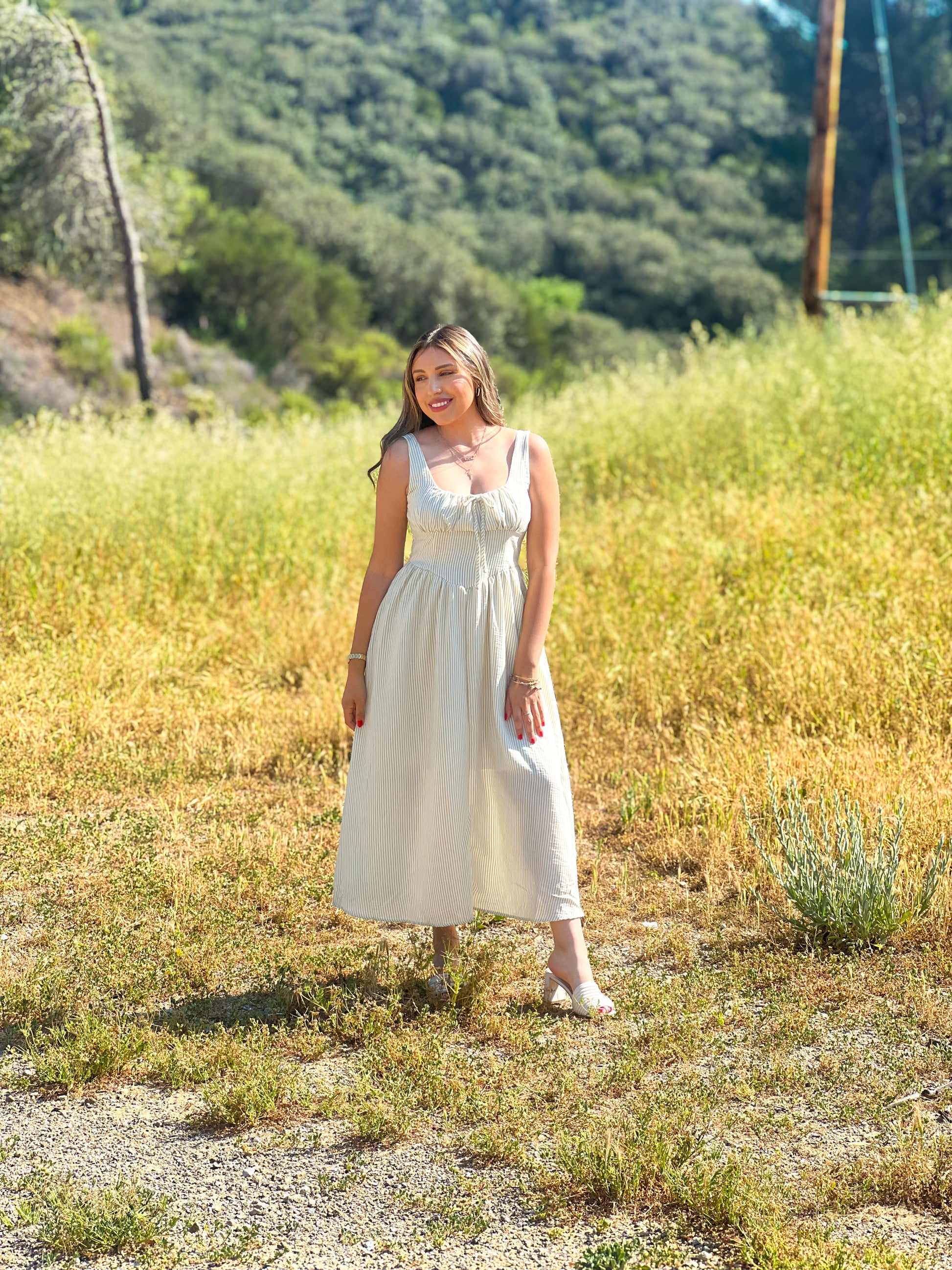 Woman in a white dress standing in a field with mountains in the background
