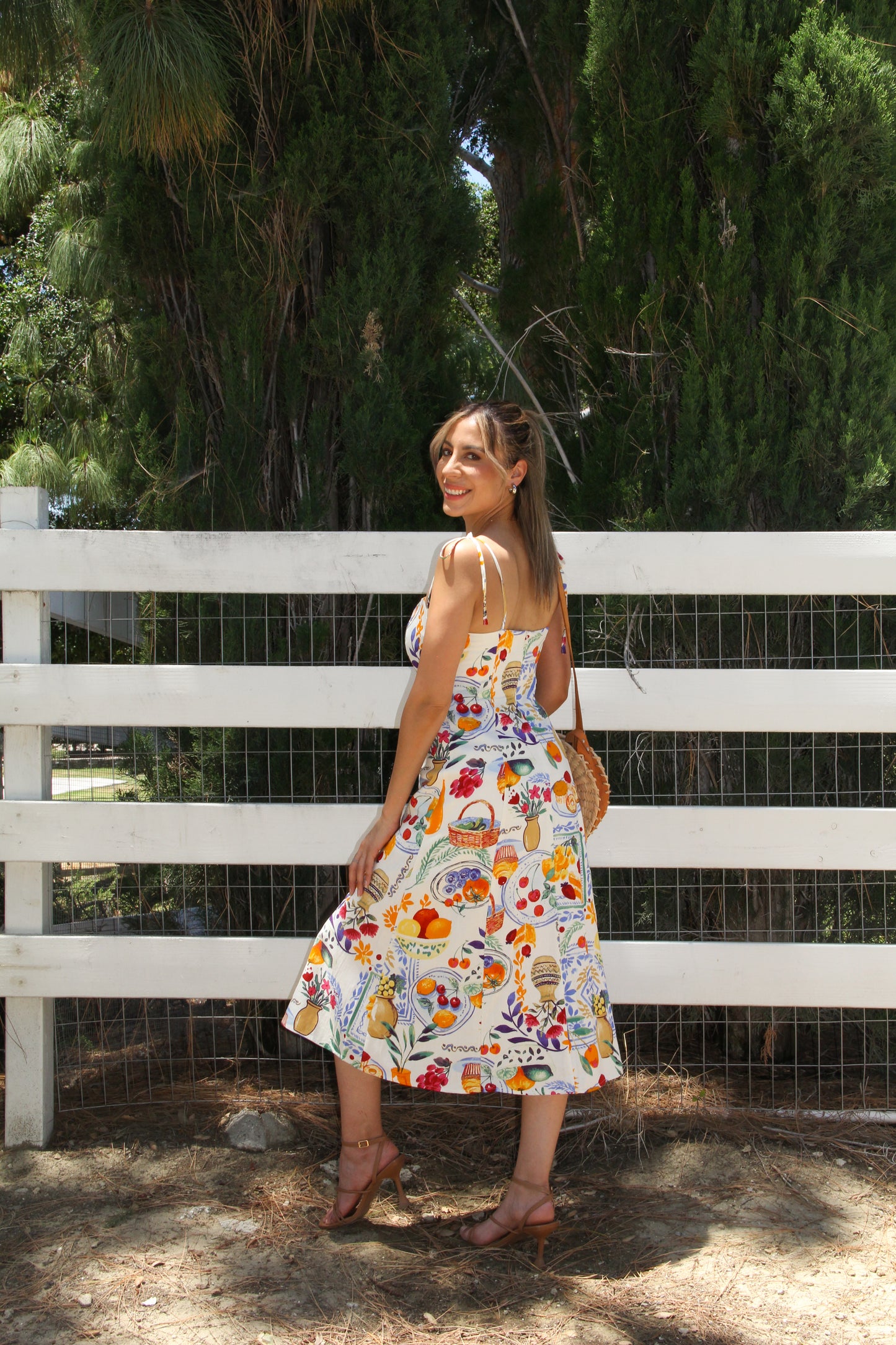 Woman in a floral dress standing in front of a white fence with greenery in the background