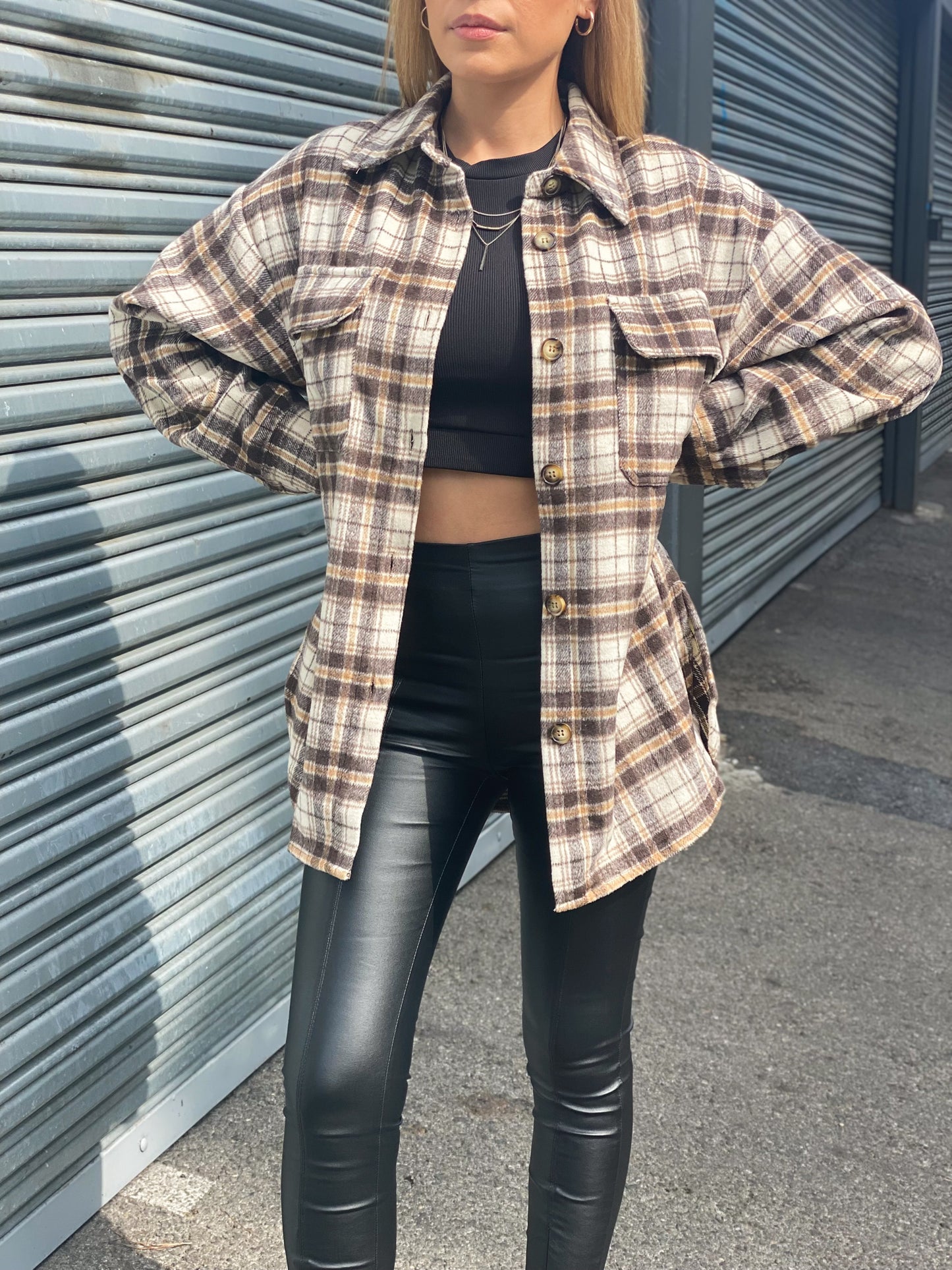 The model is standing with her hands on the side wearing an oversized brown plaid flannel. She's wearing it with a solid black top and leather leggings. The flannel has 7 buttons. 100% Polyester. The material is very soft like you're wearing a blanket. 
