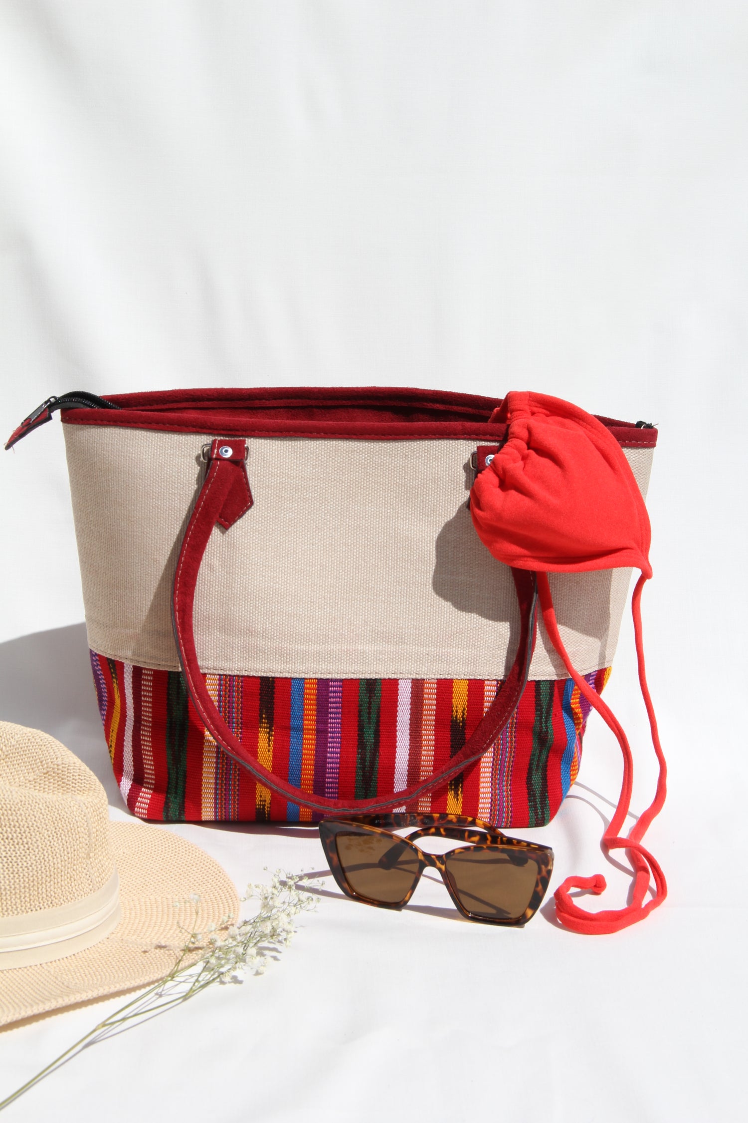 Front view of a handwoven handbag with a bottom panel of intricate Guatemalan fabric with red faux suede shoulder straps and top zipper closure to protect essential items from falling out. the prefect travel, hiking or beach bag unique bag great for your next destination boho bag and hippie style bag a great standout accessories made in Guatemala