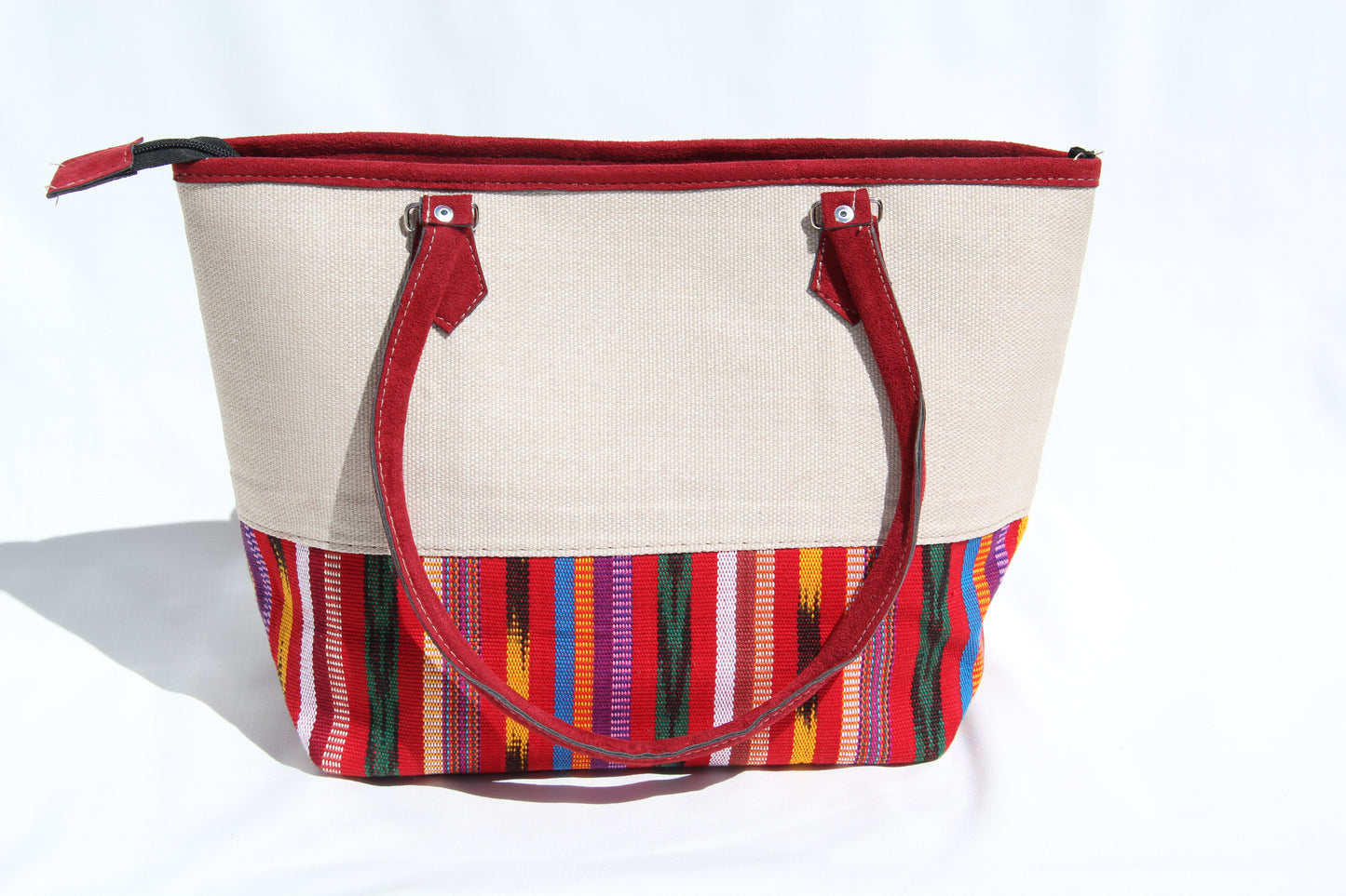 Front view of a handwoven handbag with a bottom panel of intricate Guatemalan fabric with red faux suede shoulder straps and top zipper closure to protect essential items from falling out. the prefect travel, hiking or beach bag unique bag great for your next destination boho bag and hippie style bag a great standout accessories made in Guatemala    