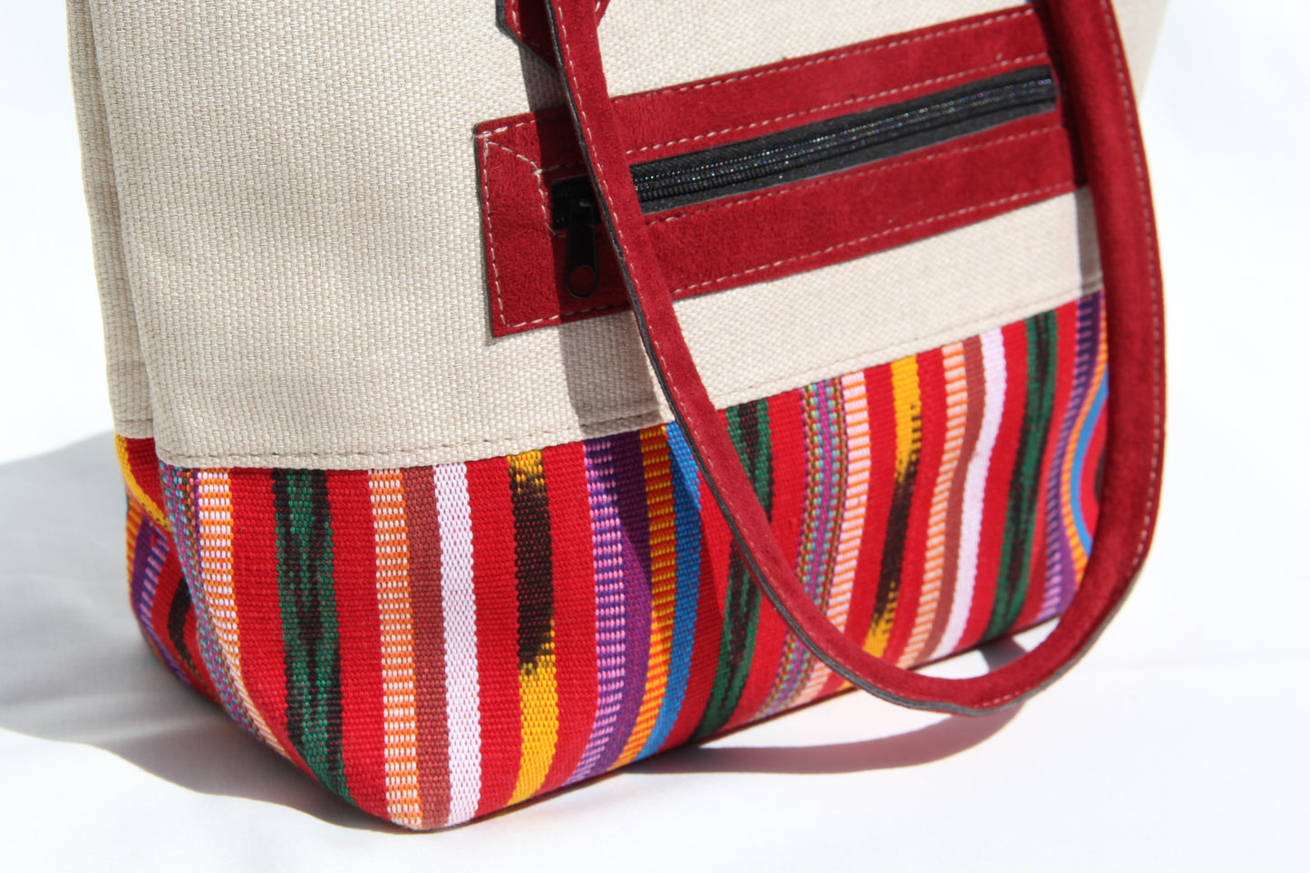 Detail view of a handwoven handbag with a bottom panel of intricate Guatemalan fabric with red faux suede shoulder straps and top zipper closure to protect essential items from falling out. the prefect travel, hiking or beach bag unique bag great for your next destination boho bag and hippie style bag a great standout accessories made in Guatemala